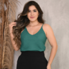 Mulher com blusa verde e calça preta, posando em um fundo neutro.