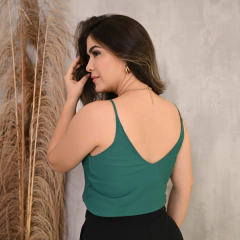 Mulher de costas usando uma blusa verde, com cabelo solto e segurando uma mecha de cabelo.