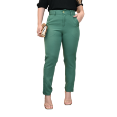 Mulher usando calça verde com blusa preta e sandália, segurando uma bolsa dourada.