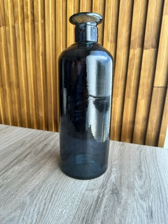 Botellón Madrid chico de vidrio oscuro sobre mesa de madera con fondo de paneles verticales de madera