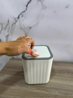 Cesto de mesada gris y blanco con tapa push, en uso, sobre una superficie de madera en el baño.