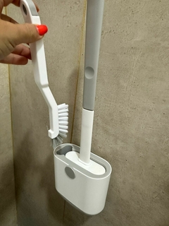 Escobilla siliconada con cepillo en soporte, ideal para limpieza de baño.