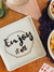 Prato para aperitivo com a frase "Enjoy it all", decorado em um ambiente acolhedor.