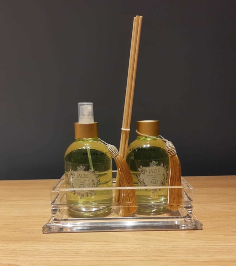 Bandeja transparente com dois frascos de difusor de ambiente Jade e dois bastões de madeira com tassel dourado sobre mesa de madeira