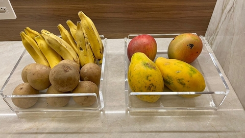 Bandeja fruteira com bananas e frutas tropicais, como mangas e mamões, em uma superfície de pedra clara.