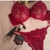 Conjunto de lingerie de renda vermelho com sutiã e duas calcinhas, acompanhado de produtos de maquiagem.