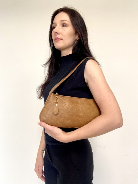 Modelo segurando uma bolsa baguete caramelo, com alça de ombro, em fundo neutro.