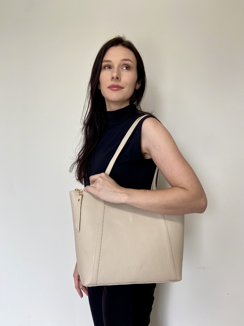 Modelo segurando uma bolsa tote luna na cor off white, com um fundo neutro.