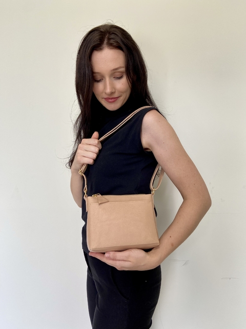 Modelo segurando a bolsa crossbody Lena Petit na cor blush, com um fundo neutro.