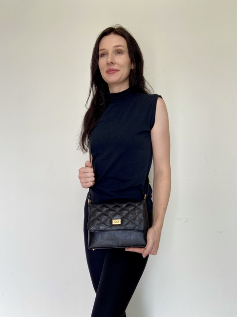 Modelo segurando a bolsa crossbody Íris Preto, com design acolchoado e detalhes em dourado, em um fundo neutro.