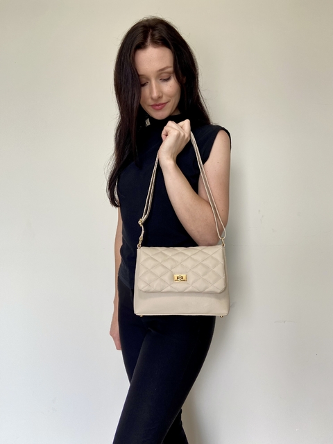Modelo segurando uma bolsa crossbody tiracolo Íris Off White, com design acolchoado e detalhes em dourado.