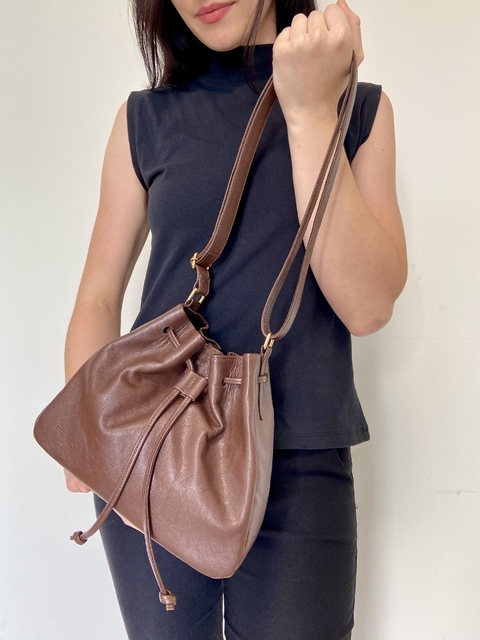 Mulher segurando uma bolsa bucket marrom, com alças longas e detalhes em couro.