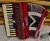 Acordeon vermelho Michael com 80 baixos, teclas brancas e pretas, colocado sobre superfície de madeira e tecido felpudo.