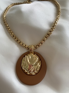 Colar dourado com pingente oval em tons marrons e detalhes brilhantes.