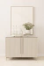 Buffet Aline de design assinado, com duas portas, decorado com garrafas, copos e um vaso com flores brancas, em um ambiente neutro.