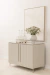 Buffet Aline de design assinado em tom claro, com duas portas, decorado com um vaso de flores e copos sobre a mesa.
