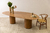 Mesa de jantar orgânica Santorini com design oval em madeira, acompanhada de vasos de flores e utensílios de mesa.