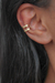 Piercing fake em formato de argola banhado a ouro 18k, posicionado na orelha de uma pessoa com cabelo escuro.
