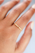 Anel minimalista cravejado com microzircônias, banhado a ouro 18k, exibido em uma mão.