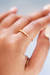 Anel minimalista cravejado com microzircônias, banhado a ouro 18k, posicionado em um dedo.