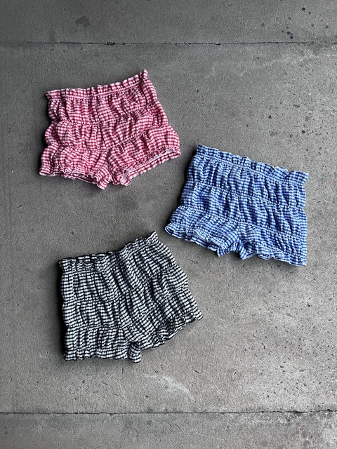 Shorts de estilo campesino con frunce en tonos rojo, azul y negro sobre una superficie gris.