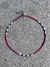 Collar Trisha con cuentas de colores rosa, rojo, negro y blanco sobre fondo de cemento.