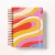 Caderno espiral com capa colorida em tons vibrantes de amarelo, vermelho, rosa, azul e bege, com elástico rosa para fechar
