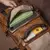 Mochila de couro marrom com compartimentos espaçosos, adequada para notebooks de até 15 polegadas.