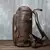 Perfil direito da mochila de couro legítimo marrom estilo vintage com bolso frontal organizador e detalhes em zíper.