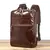 Mochila de Couro Para Notebook Café Uni 6887 Espaço para Notebook 15.6 Polegada, vista de uma ângulo lateral sobre um piso de madeira e fundo branco