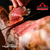 Um presunto cru Jamón Serrano sendo fatiado com uma faca, destacando sua textura e cor.