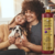 Um casal sorridente segurando um cachorro em um ambiente aconchegante, com o Shampoo Clareador Tonalizante Ametista Bambu Mossô 1L ao lado.