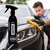 Frasco de spray de cera carnaúba NATIVE da VONIXX em primeiro plano, com um homem limpando a parte frontal de um carro preto.