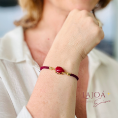 Pulseira cordão com pingente de gota vermelha, usada no pulso de uma mulher.