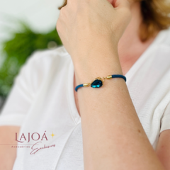 Pulseira cordão com pingente em formato de gota azul, usando uma mulher com camiseta branca.