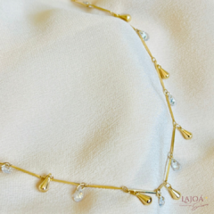 Colar longo banhado com gotas e cristais em fundo claro.