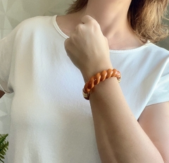 Bracelete de resina laranja com detalhes em ouro, exibido no pulso de uma pessoa.