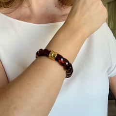 Bracelete de resina marrom com detalhe em ouro, usado no pulso de uma pessoa.