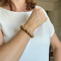 Bracelete de resina na cor bege com detalhes em ouro, sendo exibido no pulso de uma mulher.