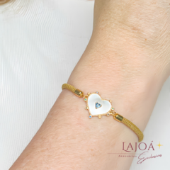Pulseira cordão com coração em madrepérola, adornada com detalhes coloridos, em um pulso feminino.