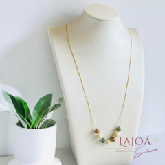 Colar longo de jade e calcita com banho de ouro, exibido em um suporte elegante.