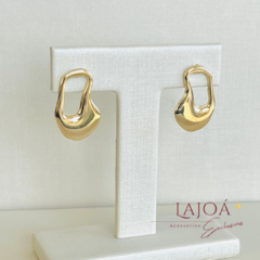Brinco argola orgânica pequeno em banho de ouro exposto em suporte branco.