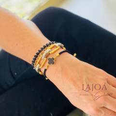 Pulseira Trevo em destaque, e contas de cristal em preto e dourado, usada no pulso de uma mulher.