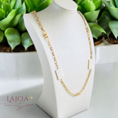 Colar corrente em madrepérola e citrino, exibido em um suporte elegante, com fundo de plantas verdes.