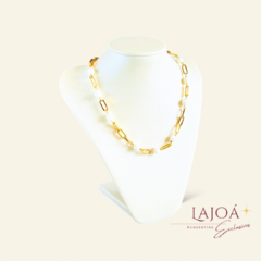 Colar corrente com esferas em madrepérolas, apresentando detalhes em dourado, exibido em um suporte branco.
