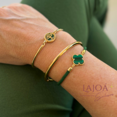 Pulseira Trevo em destaque, com detalhes em verde e dourado, adornando um braço.
