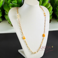 Colar longo com pedras de citrino em um suporte branco, com detalhes em dourado.