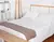 Manta pie de cama tejida "La Bastilla" sobre una cama blanca con almohadas.