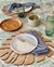 Posafuentes de madera en forma de hoja de monstera, con platos, cubiertos y servilletas sobre una mesa decorada con hojas.