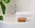 Toalla de rostro blanca "Fantasia" apilada junto a jabones en un lavabo moderno.